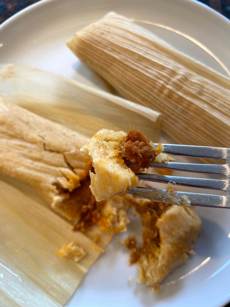 fork stabbing piece of tamale above a plate with tamales