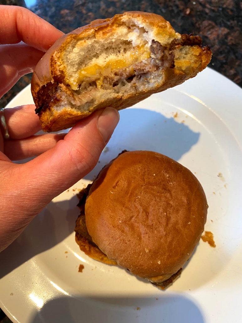 hand holding partially eaten air fried white castle slider above another slider on a plate