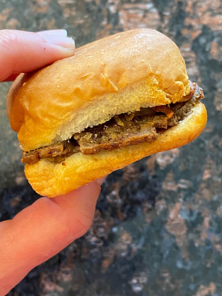 hand holding white castle slider above marble counter