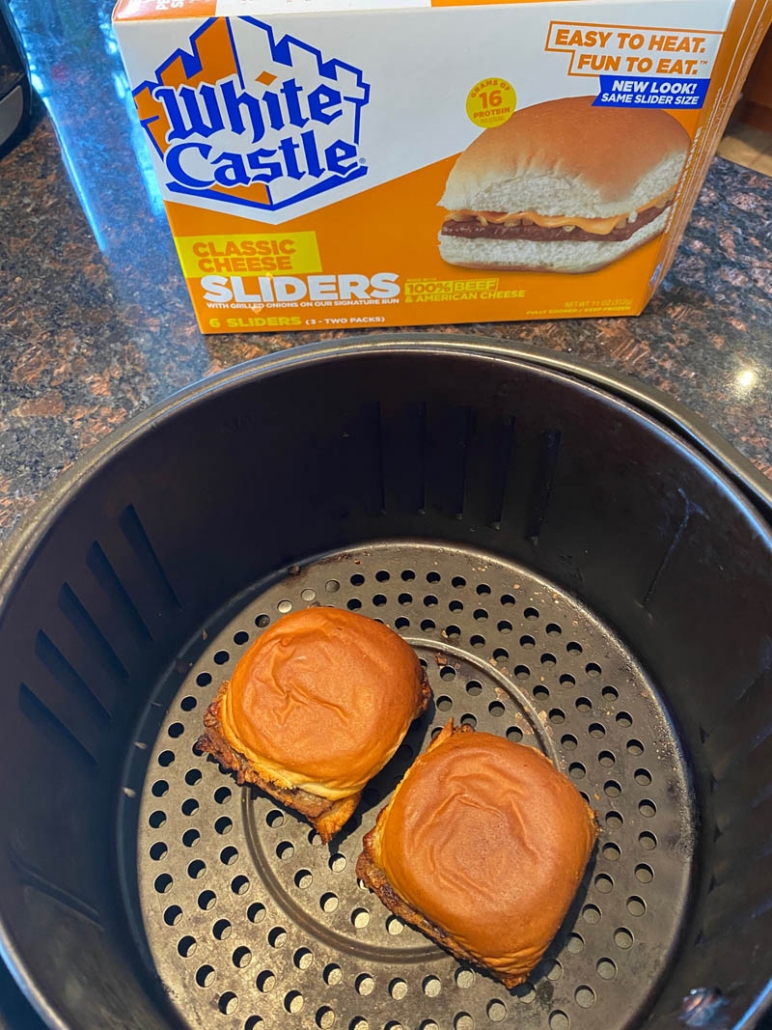 two white castle sliders inside air fryer with package of sliders behind