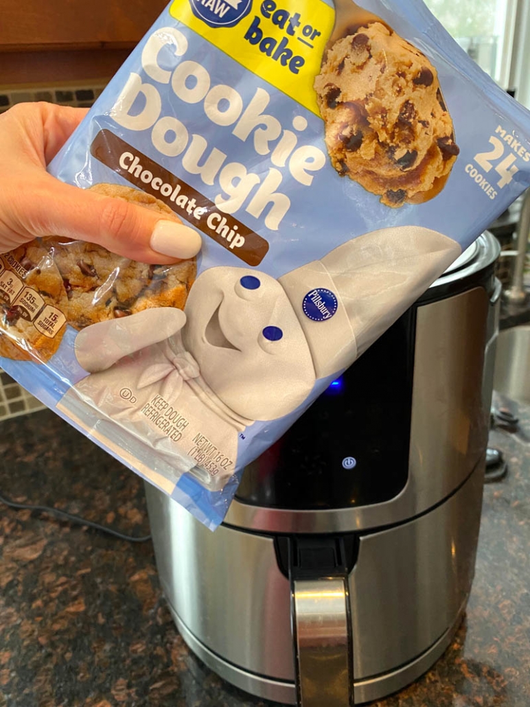 hand holding package of pillsbury cookie dough in front of the air fryer
