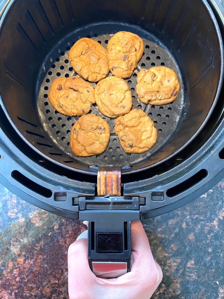 hand holding air fryer basket with cooked chocolate chip cookies inside