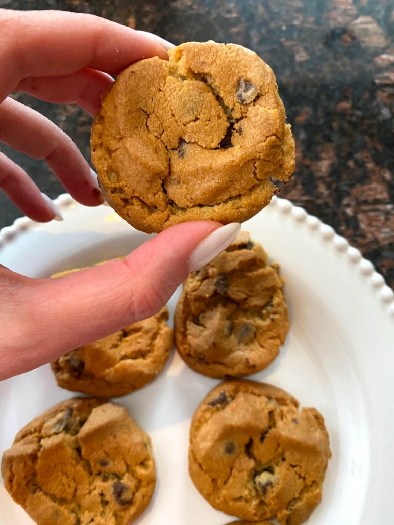 hand holding chocolate chip cookie above plate of cookies