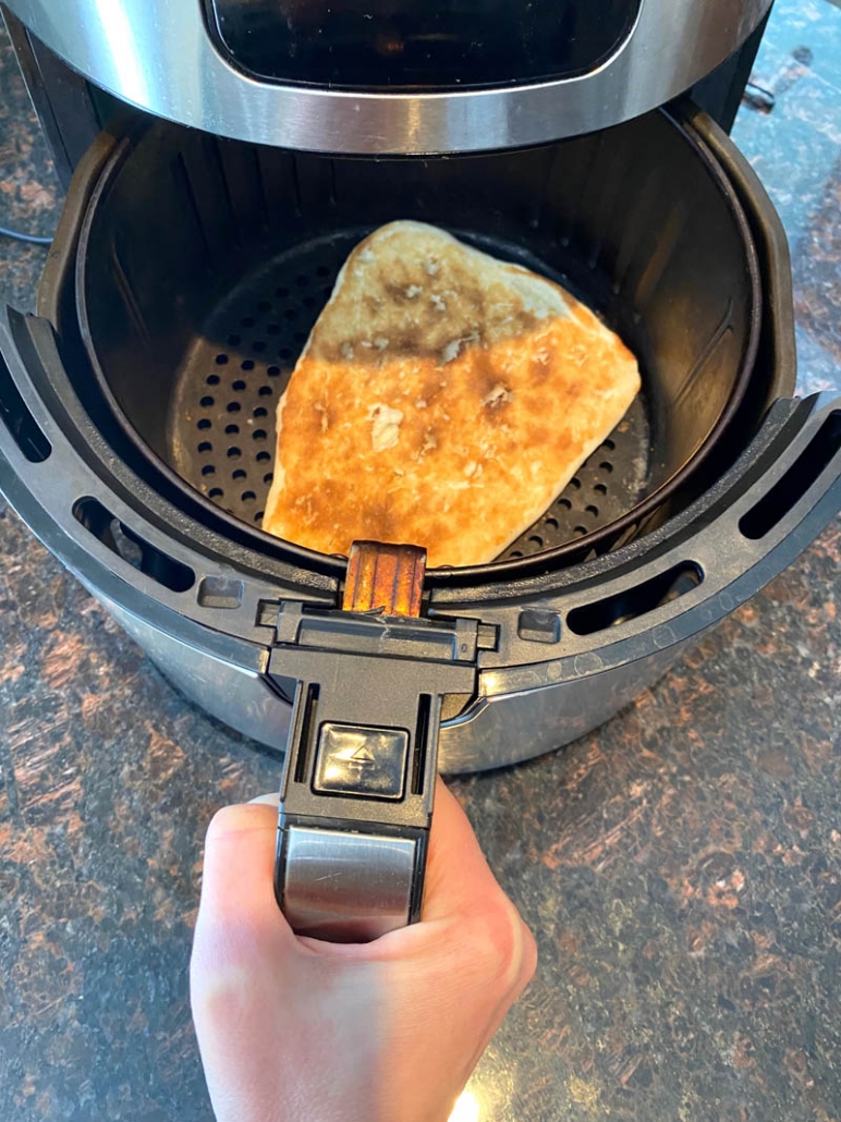 inserting air fryer basket into air fryer with naan bread