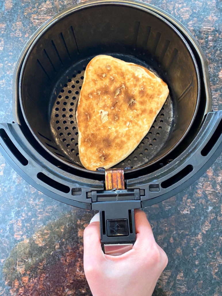 hand holding air fryer basket with frozen naan bread