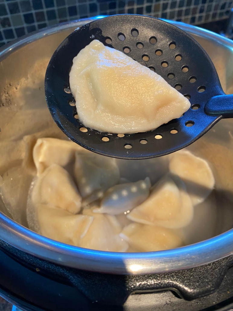 slotted spoon picking up pierogi from inside instant pot