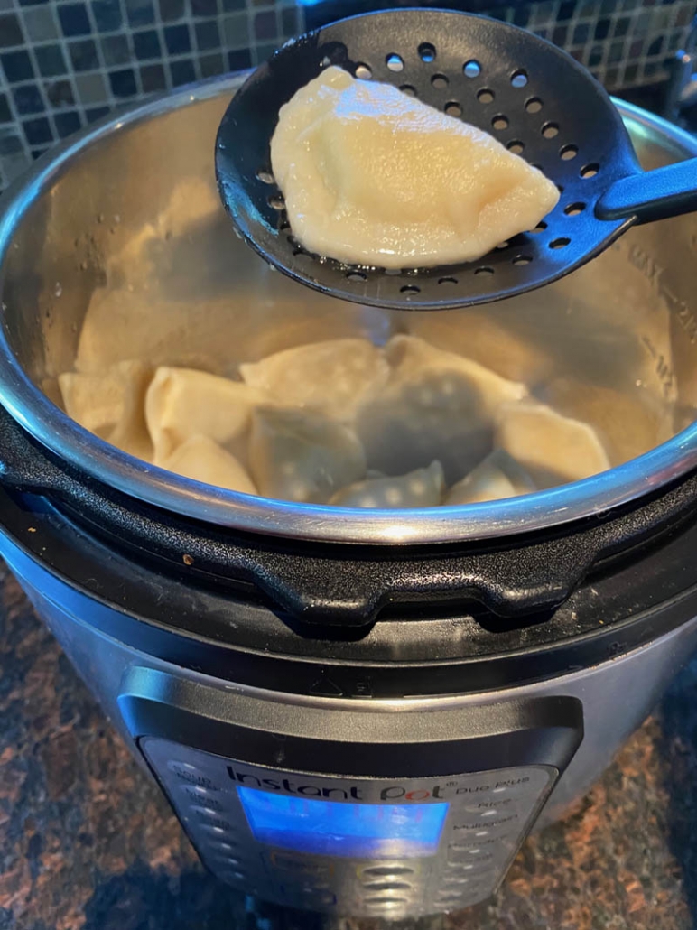 slotted spoon picking up pieorgi from inside instant pot