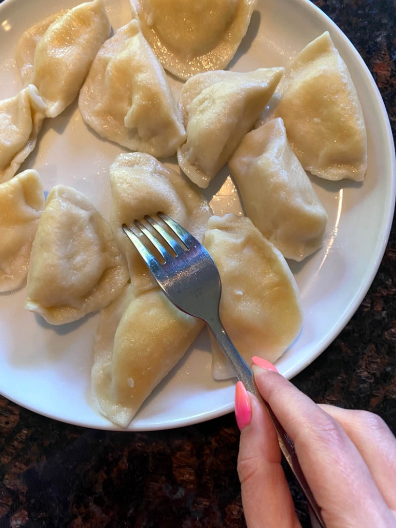 fork stabbing pieorgi on a plate filled with pierogies