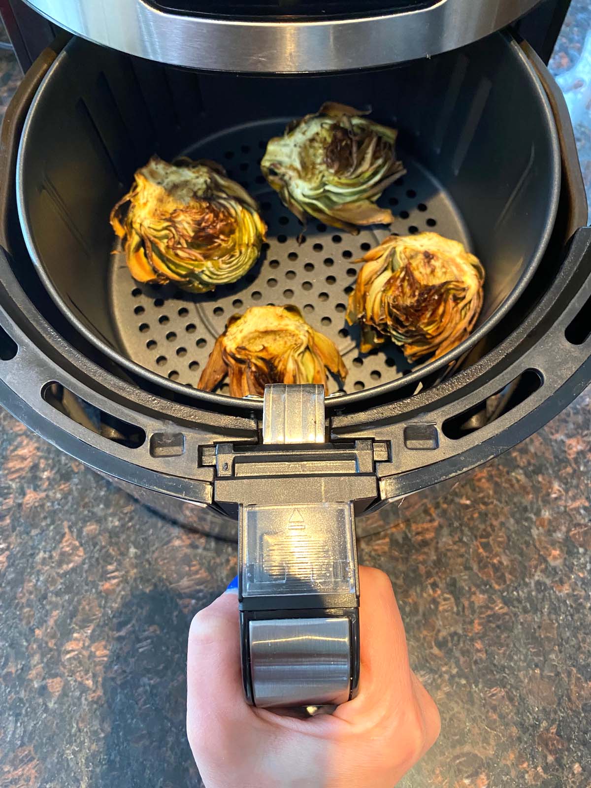 Basket of a table top convection oven with 4 artichoke halves cooked crispy.