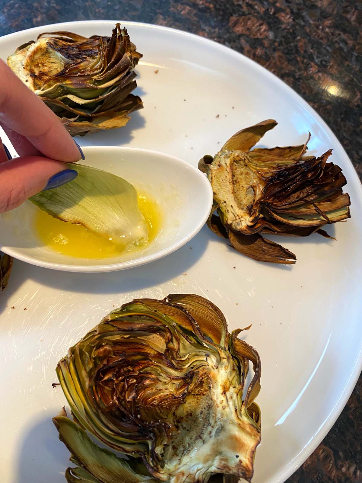 Cooked artichoke halves on a large plate with butter for dipping.