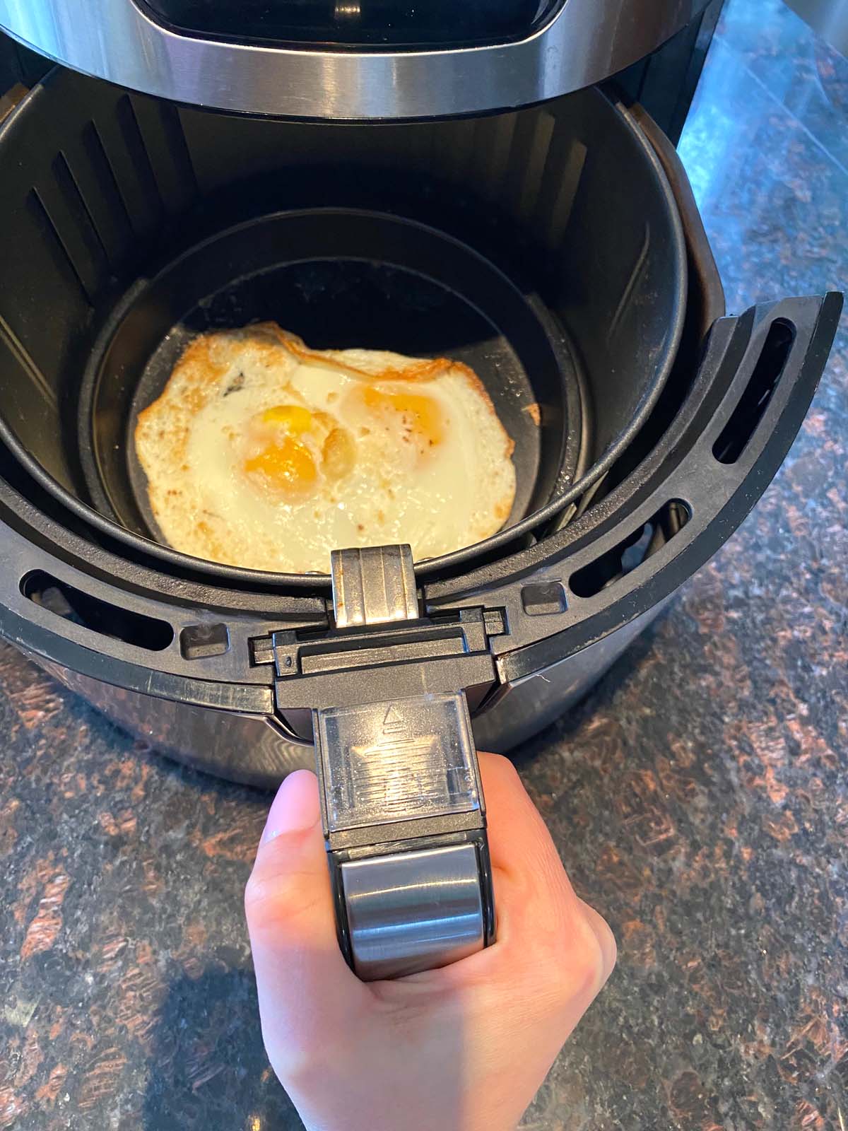 2 eggs in air fryer with the basket being removed.