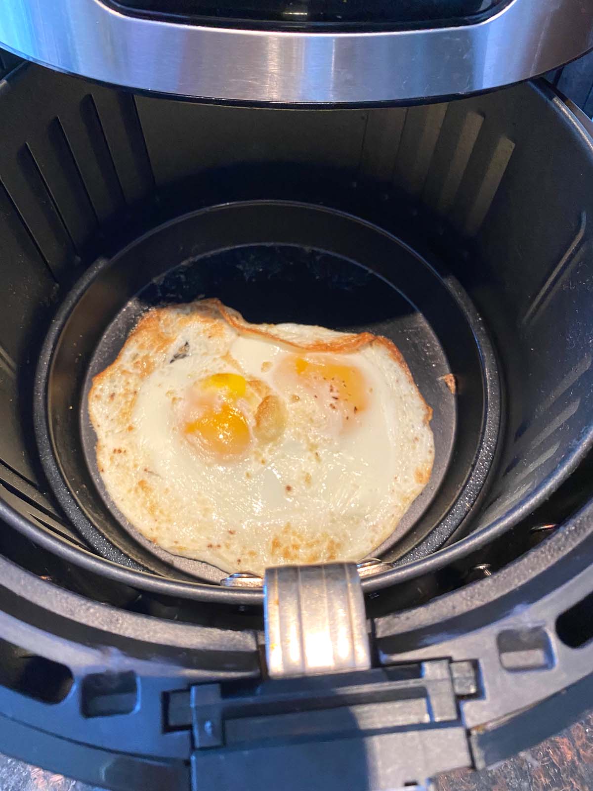 2 cooked sunny up eggs in an air fryer basket. 