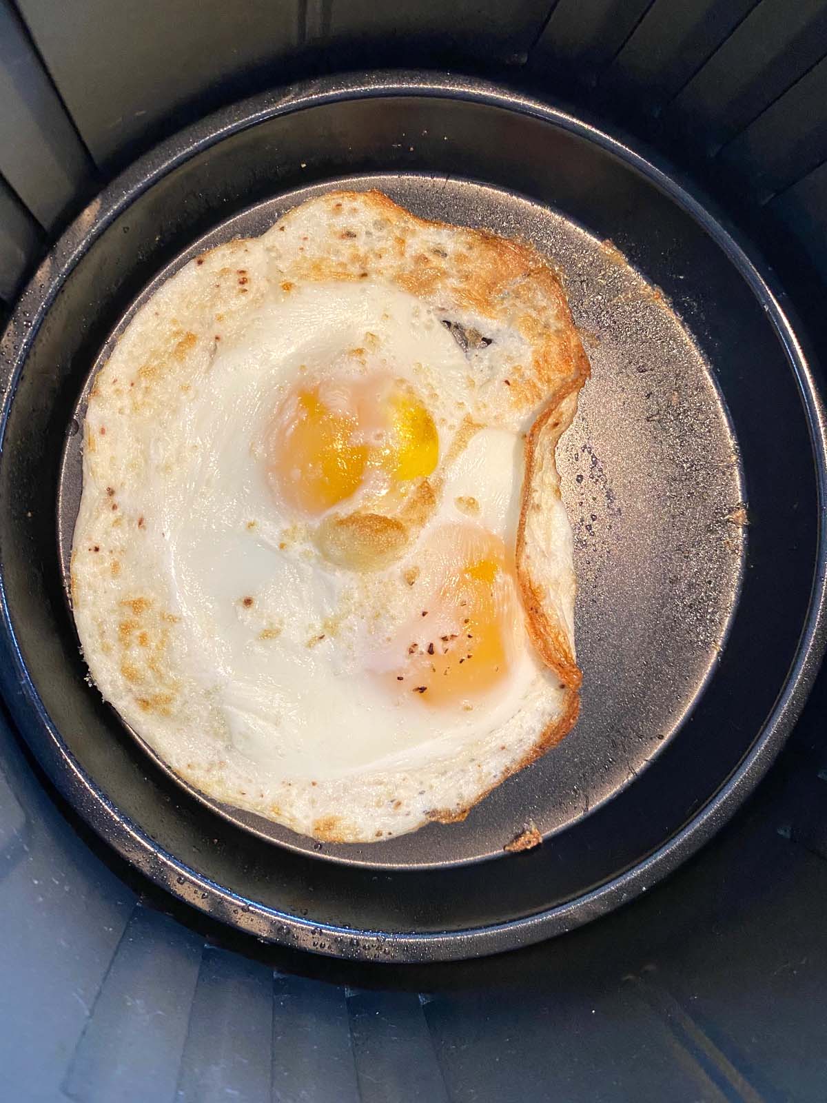 A pan inside a fryer basket with 2 eggs cooked inside.