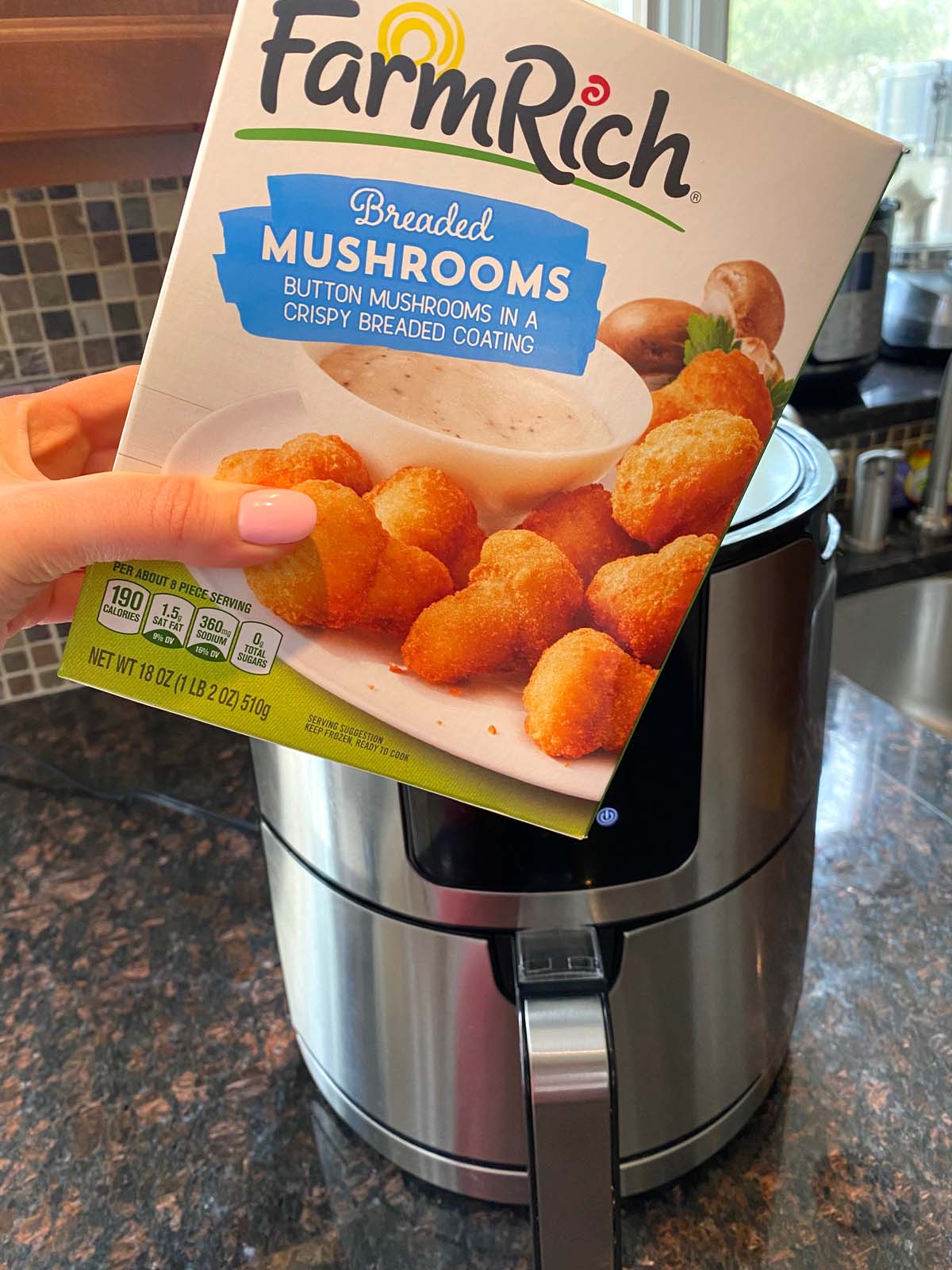 A box of frozen breaded mushrooms being held up in front of an air fryer.