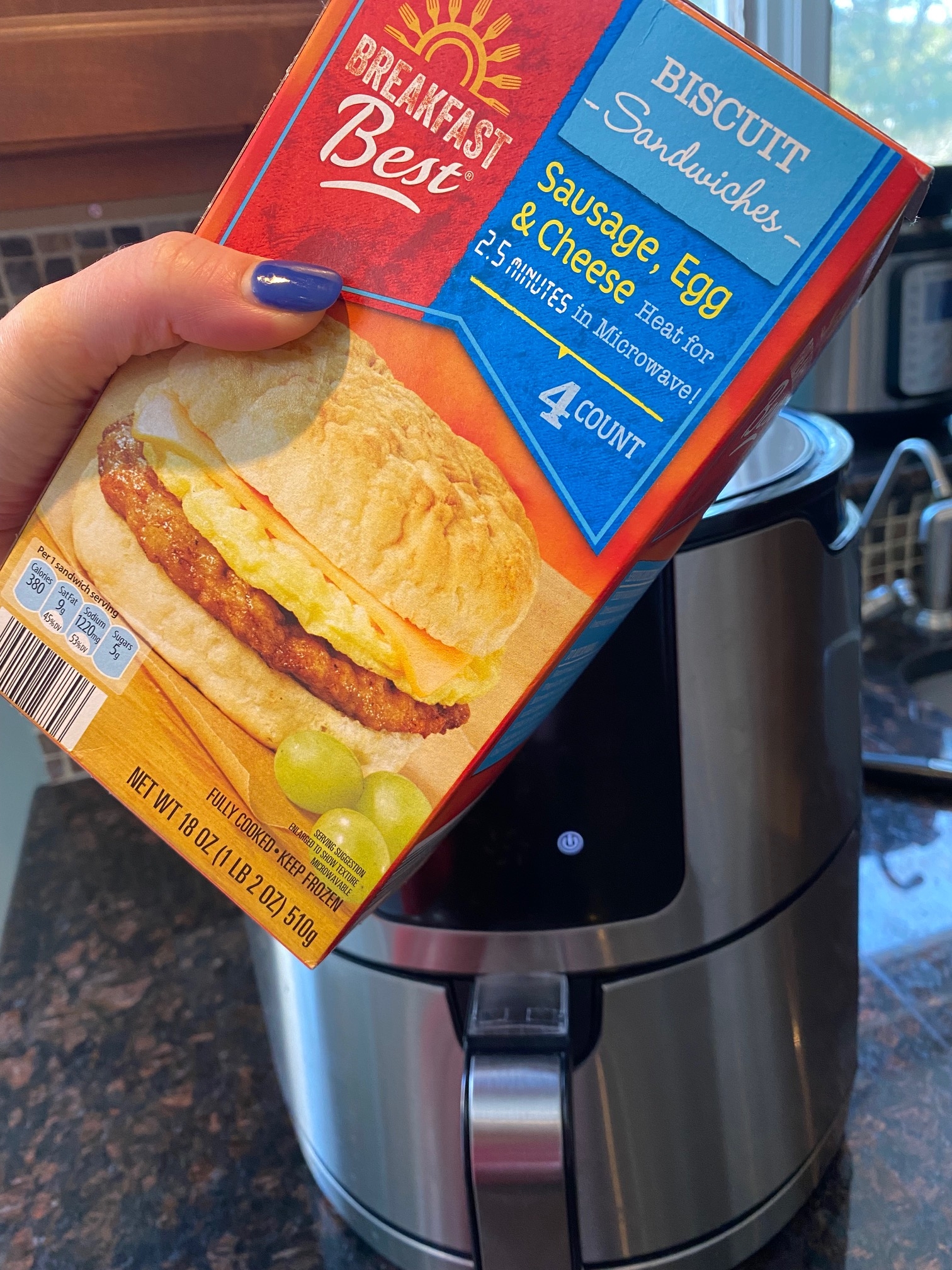 A box of frozen breakfast sandwiches in front of an air fryer. 