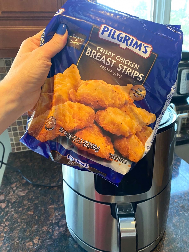 hand holding bag of frozen chicken strips in front of air fryer