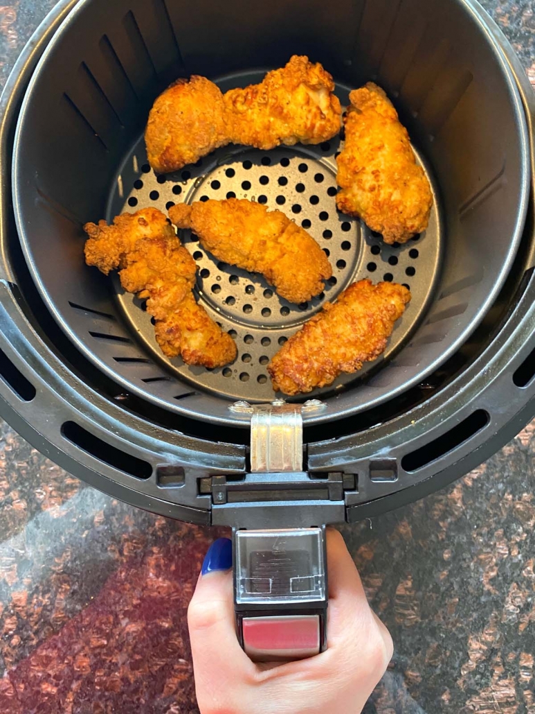 hand holding air fryer basket with multiple chicken wings