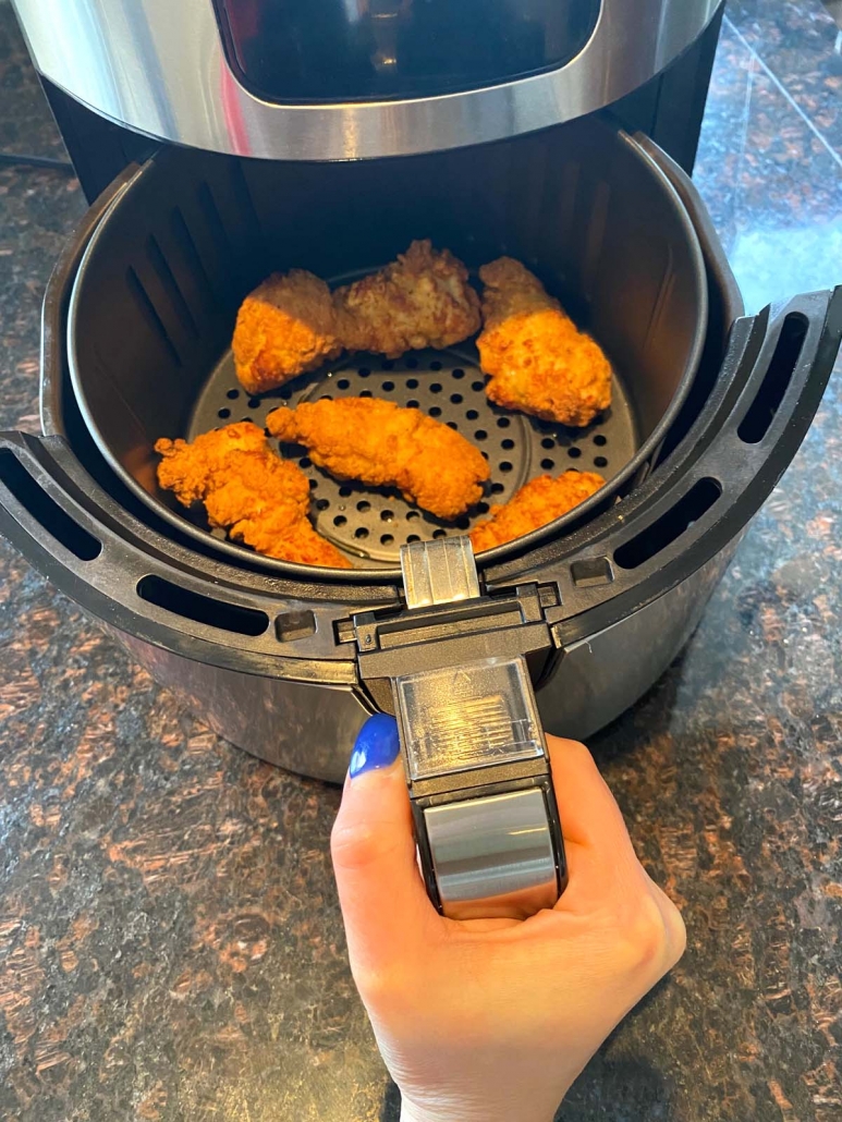 hand holding air fryer basket on the counter with some chicken strips inside