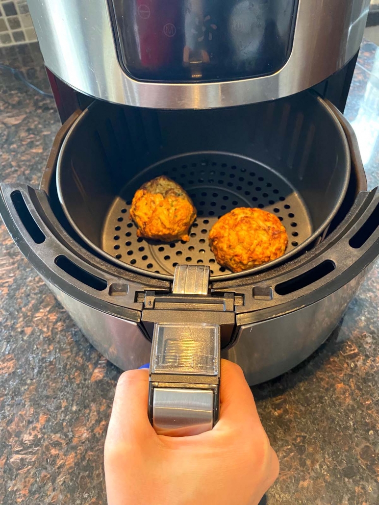 hand holding air fryer basket with 2 frozen crab cakes inside