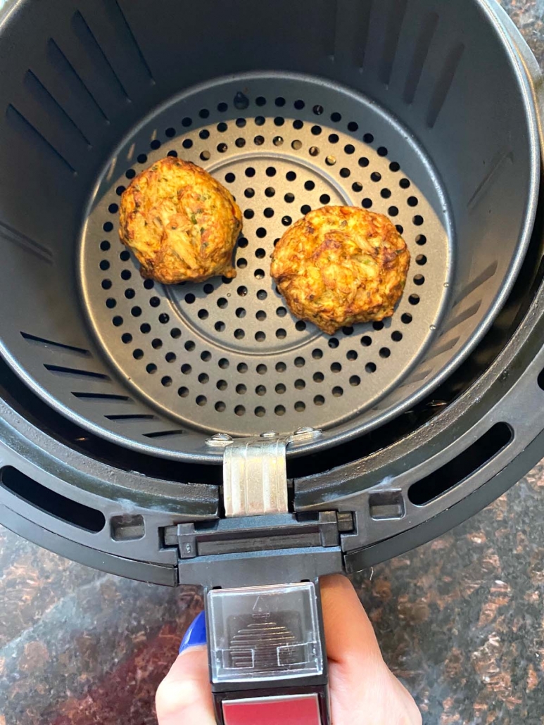 hand holding air fryer basket with frozen crab cakes