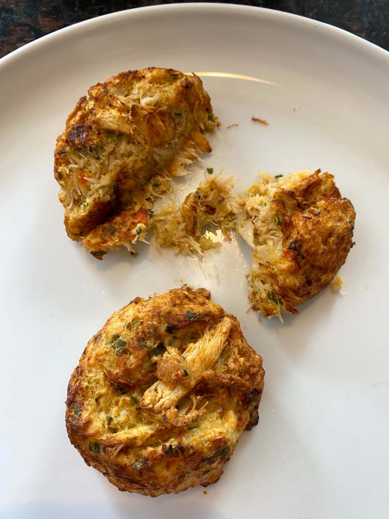 two air fried crab cakes on a plate with one cut in half