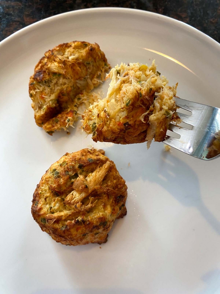 fork holding piece of crab cake over plate with rest of crab cakes