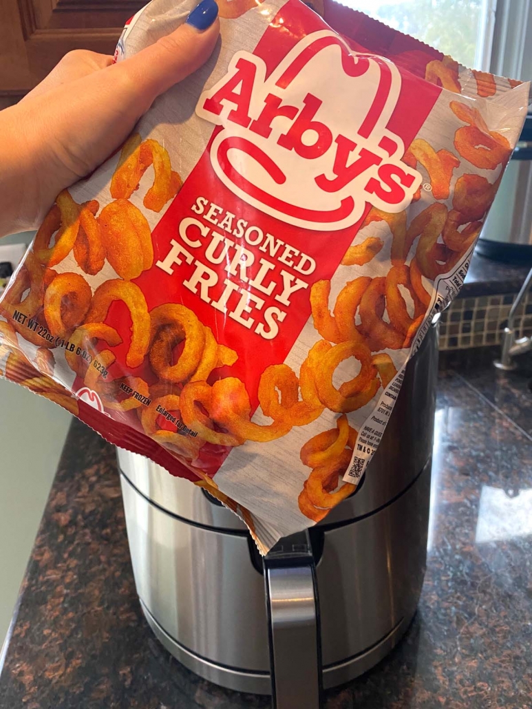 hand holding bag of curly fries in front of the air fryer