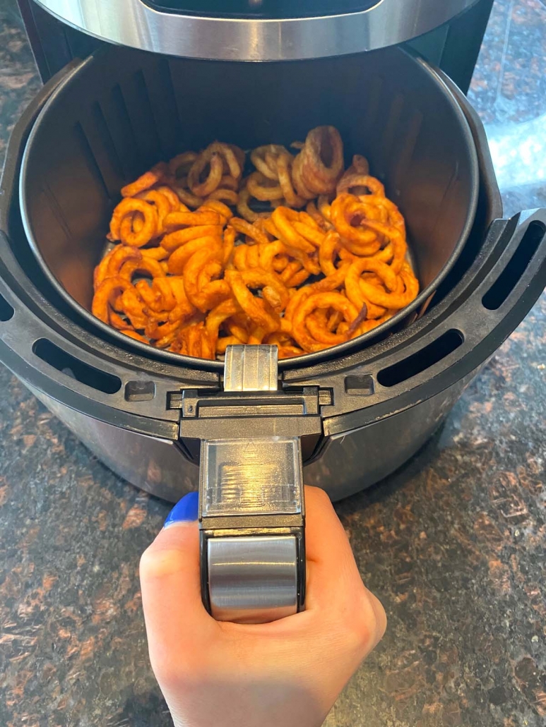 hand holding air fryer with curly fries inside