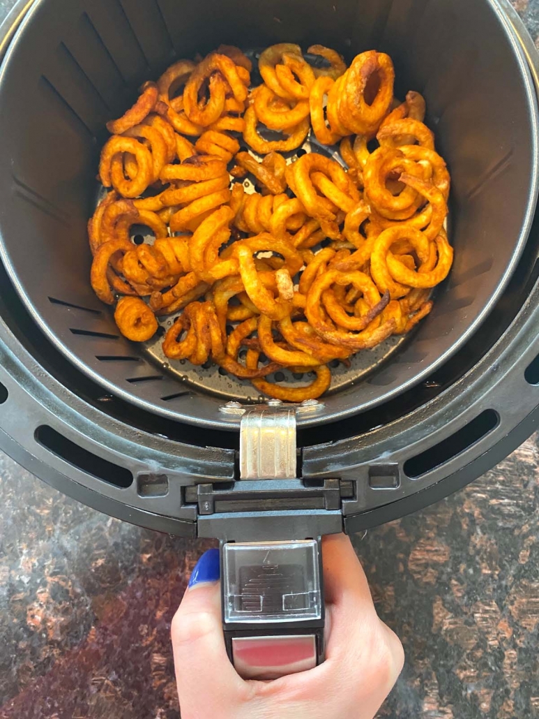 hand holding air fryer basket filled with crispy curly fries