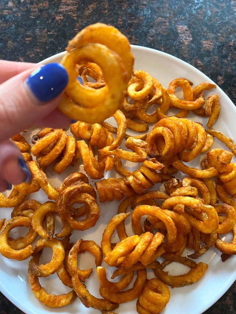 hand holding curly fry above plate of air fried curly fries
