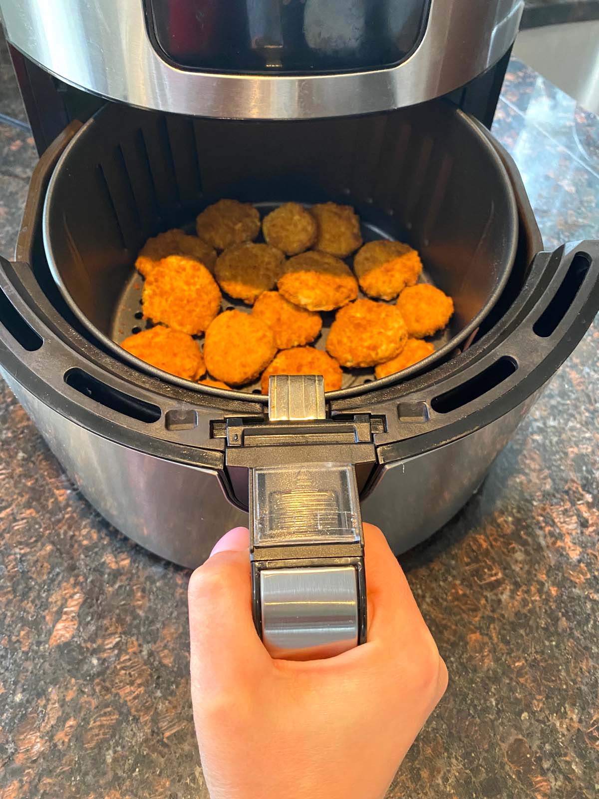 Hand pushing basket of frozen pickle chips into air frying machine.