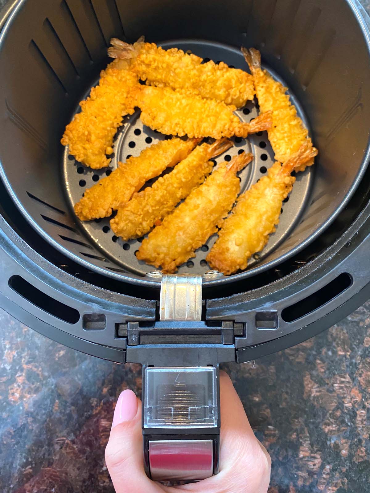 Air fryer basket being removed to show cooked crispy tempura shrimp.