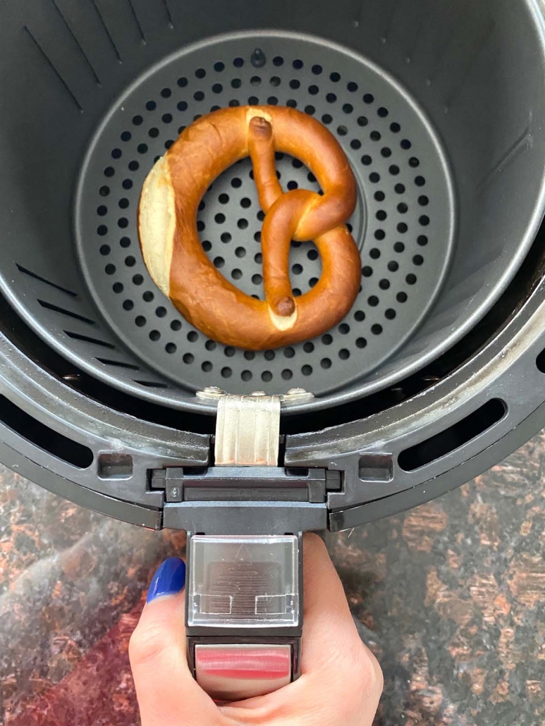 hand holding air fryer basket with soft pretzel inside