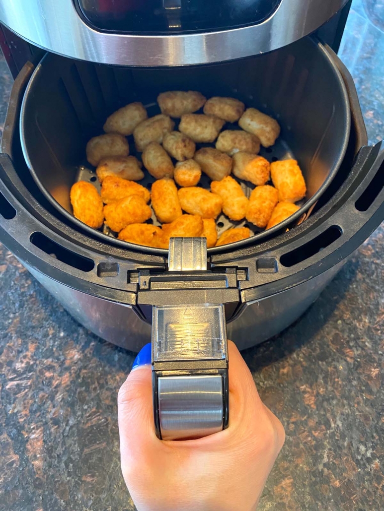 hand holding air fryer basket filled with veggie tots