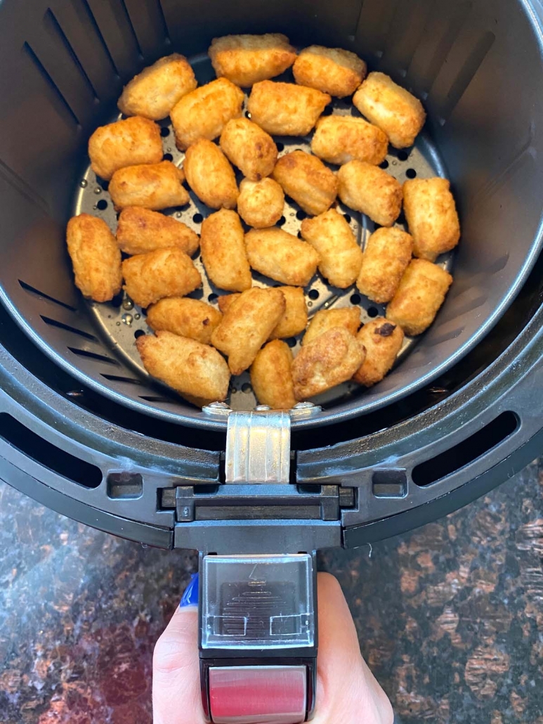 hand holding air fryer basket with air fried veggie tots inside