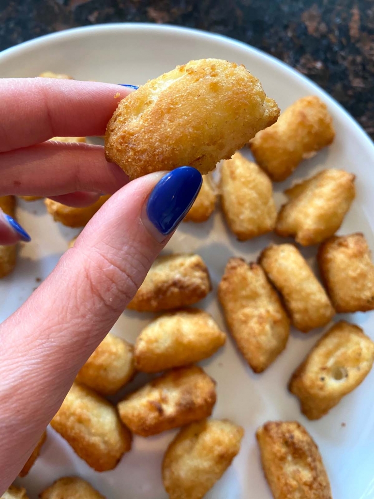 hand holding single veggie tot over plate of air fried tots