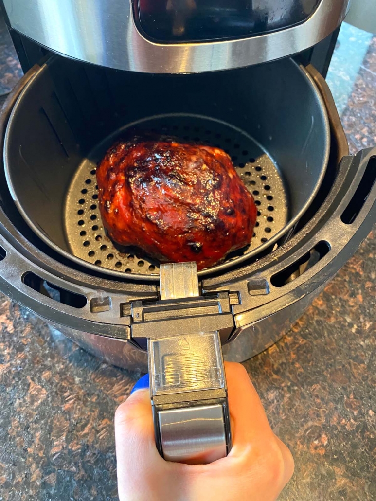 hand holding air fryer with meatloaf inside