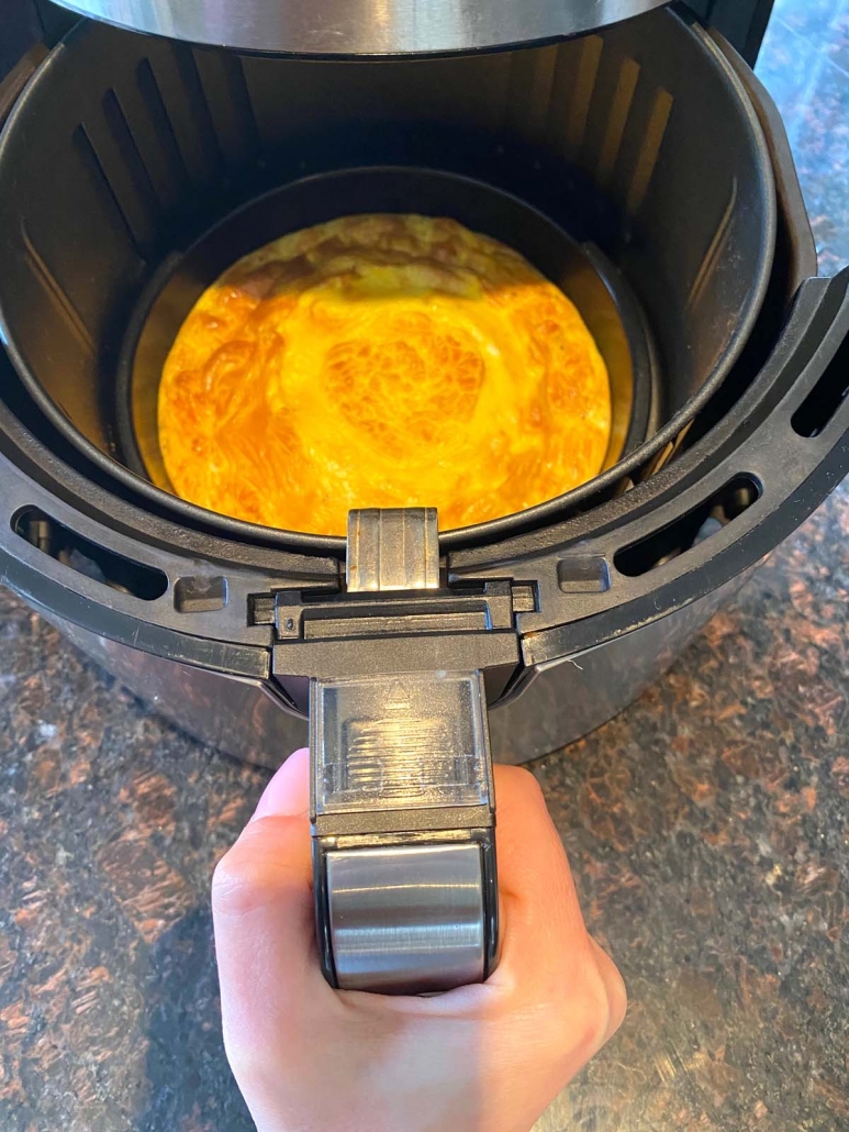 hand holding air fryer basket with omelette inside