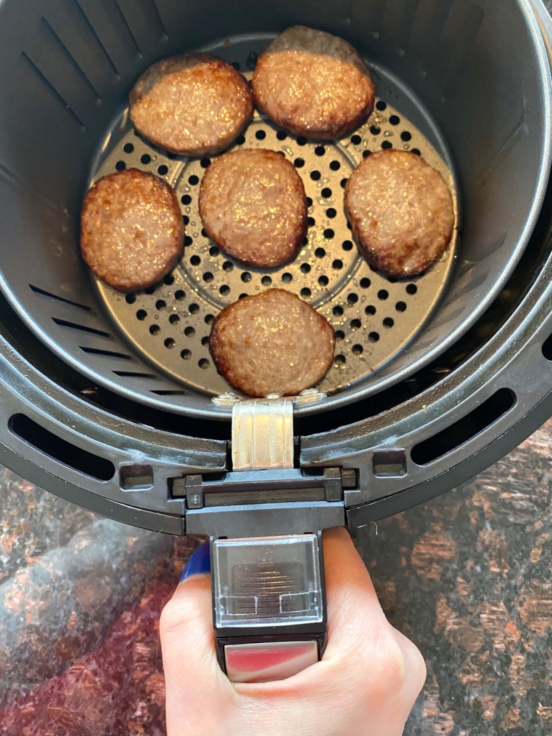 hand taking out air fryer basket with air fried sausage patties inside