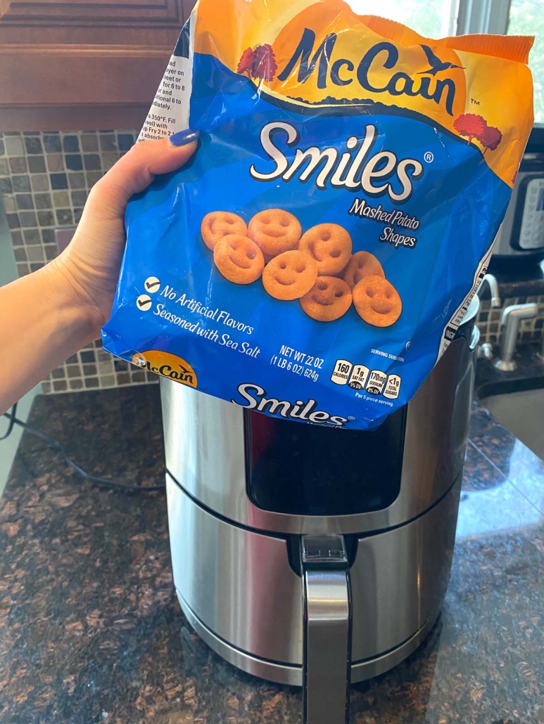 hand holding bag of frozen smiley fries in front of air fryer