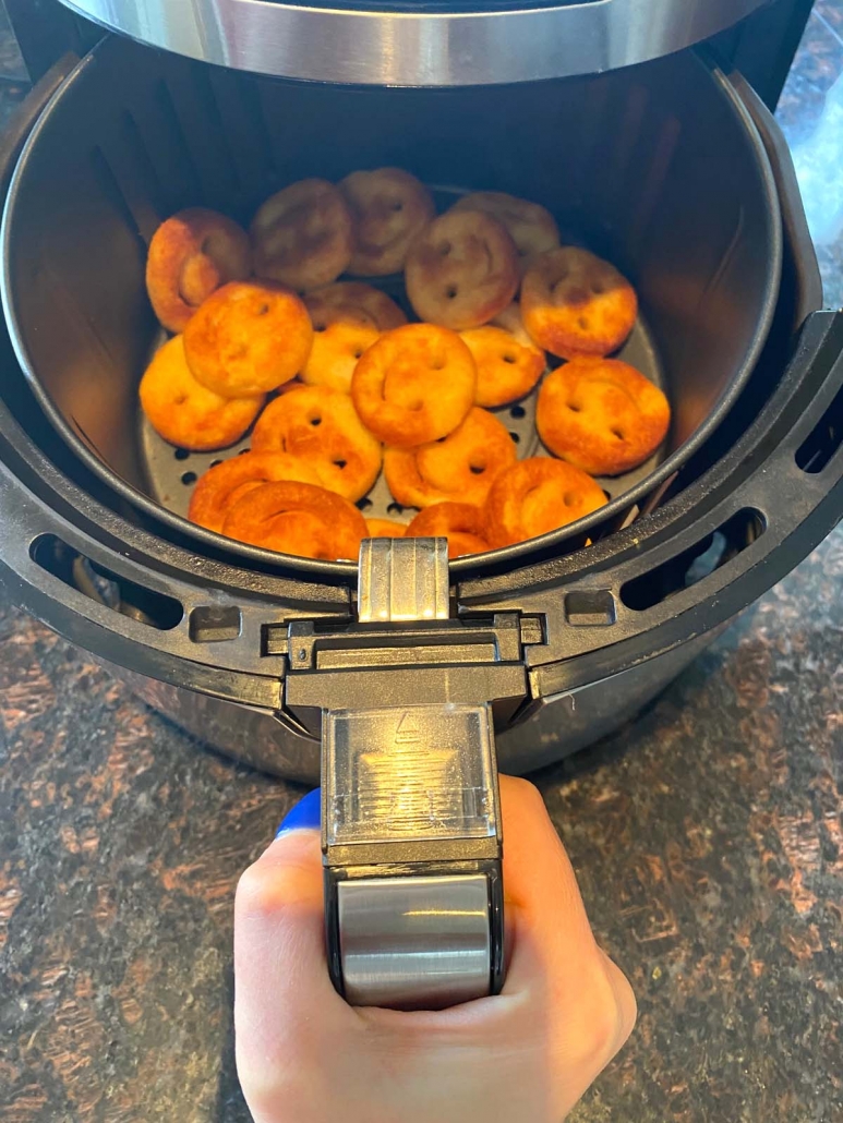 hand holding air fryer basket with smiley fries