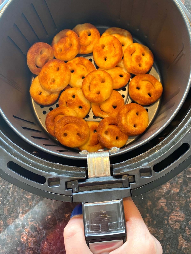 hand pulling out air fryer basket filled with cooked smiley fries