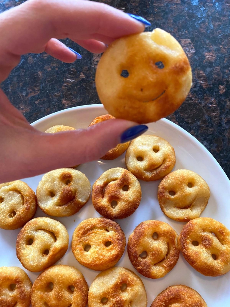 hand holding a single air fried smiley fry over plate filled with more fries