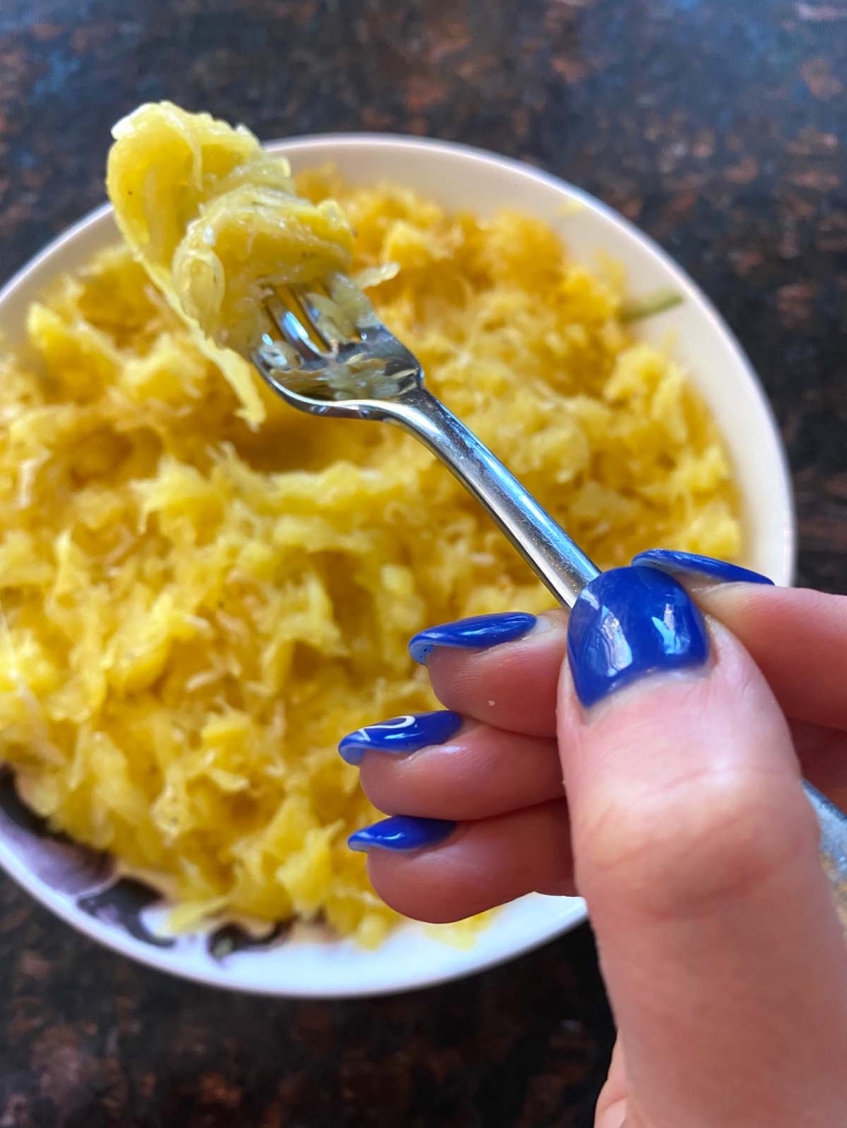 hand holding a fork above plate with cooked spaghetti squash strands