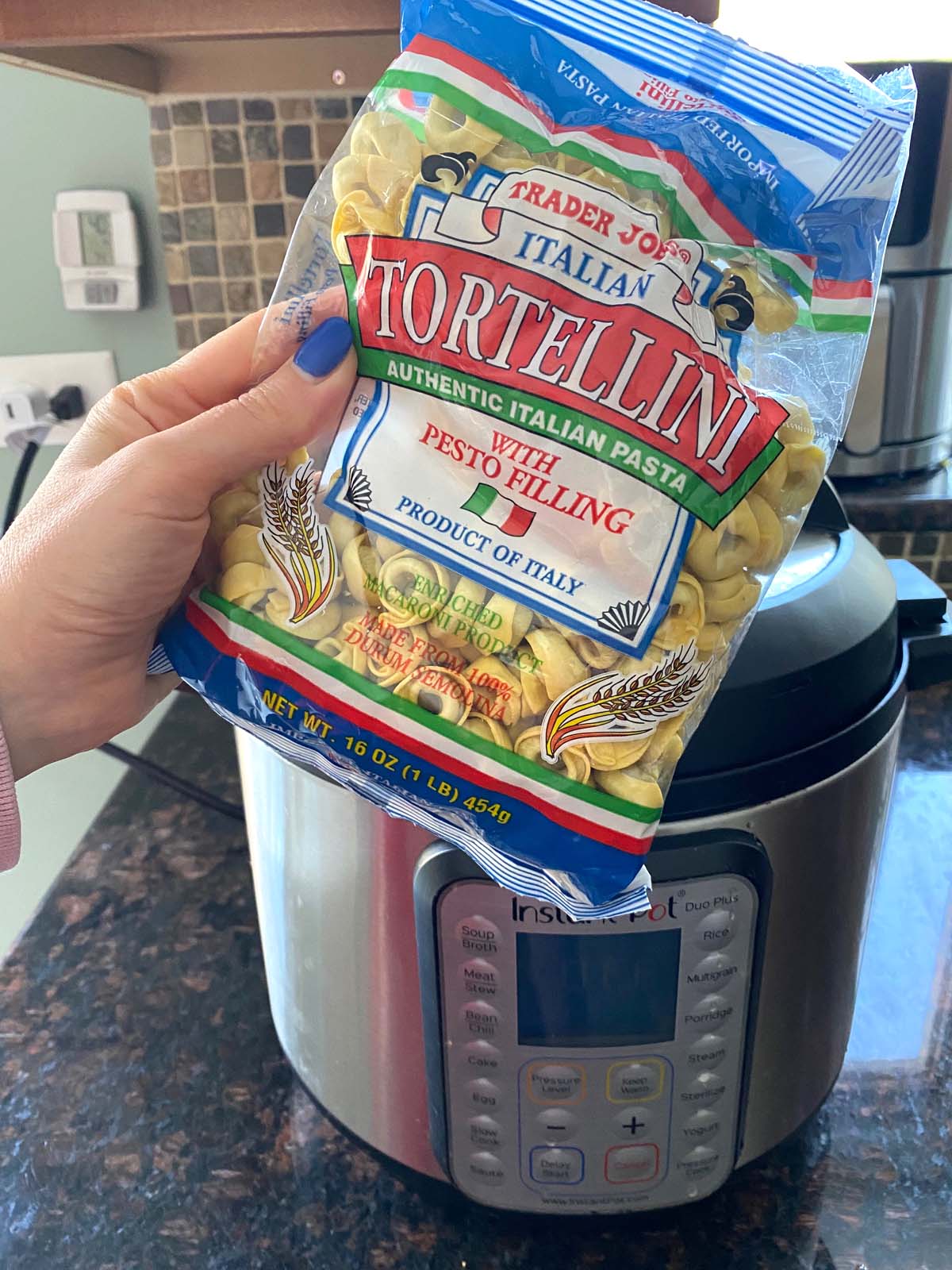 A bag of dried tortellini being held up in front of an instant pot.