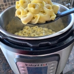 A spoon of cooked tortellini being held over an instant pot full of cooked tortellini.