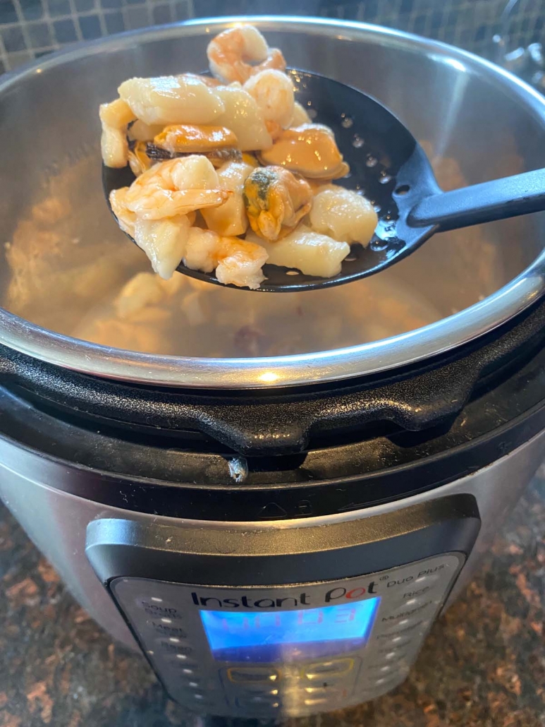 slotted spoon scopping up cooked seafood medley from the instant pot
