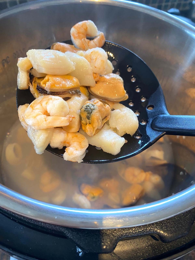 close up of slotted spoon holding seafood medley cooked in instant pot 