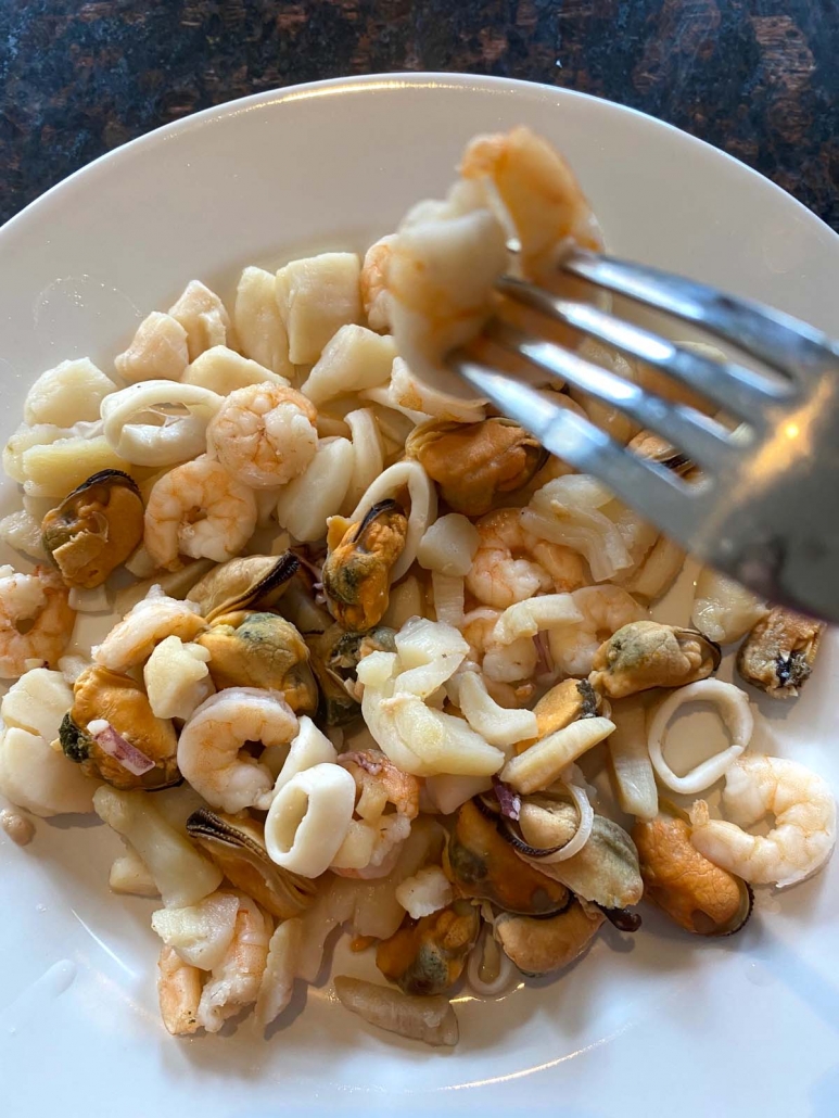 fork picking up piece of seafood medley above plate