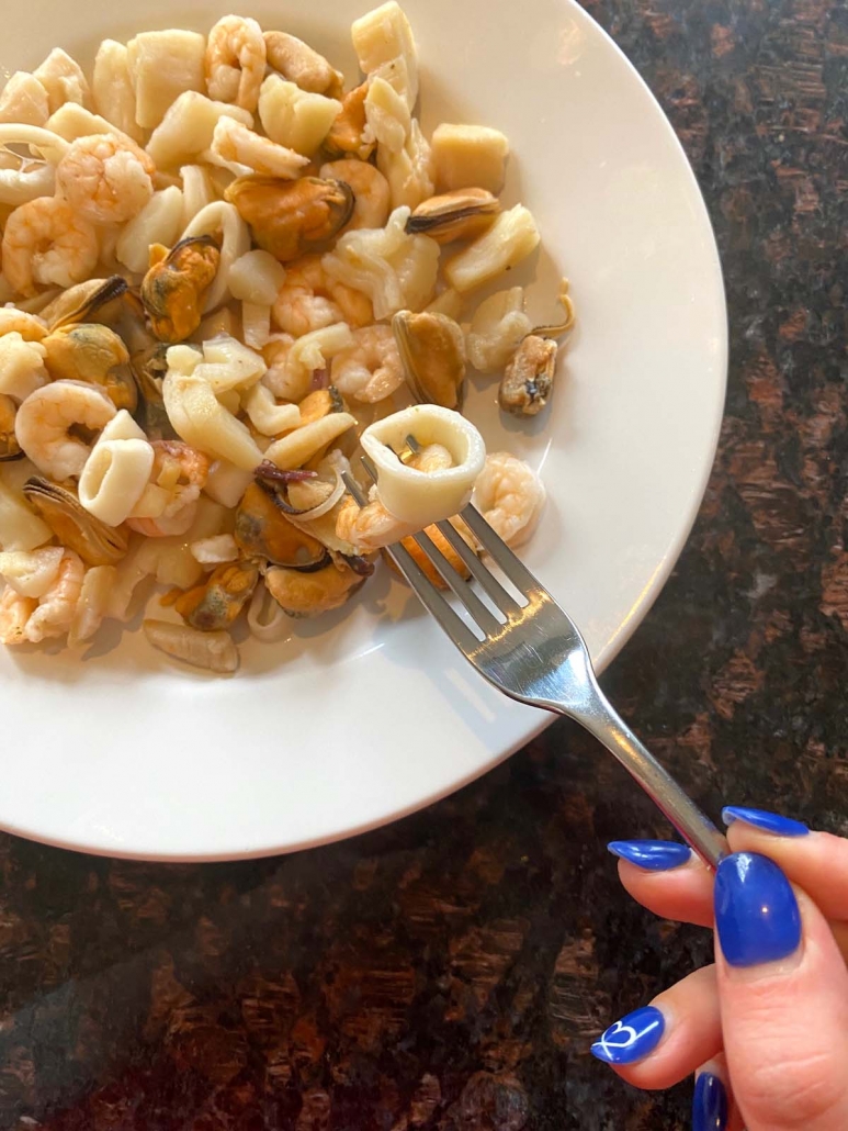 hand holding fork over plate filled with instant pot cooked seafood medley